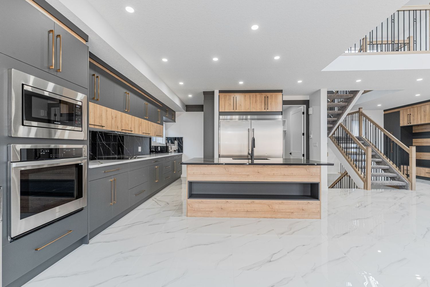 Modern kitchen with gray cabinets, wood accents, stainless steel appliances, marble floors, and a large island.