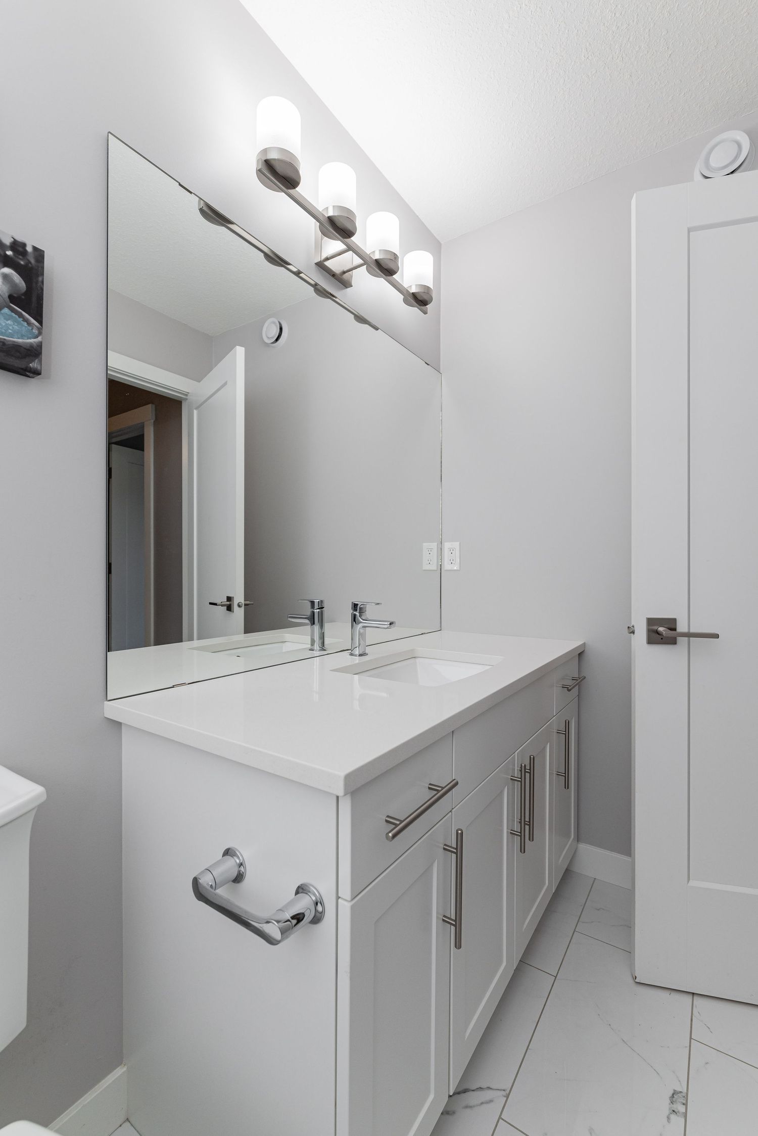 Modern white bathroom vanity with dual sinks, large mirror, chrome fixtures, and bright lighting on white tile floors.