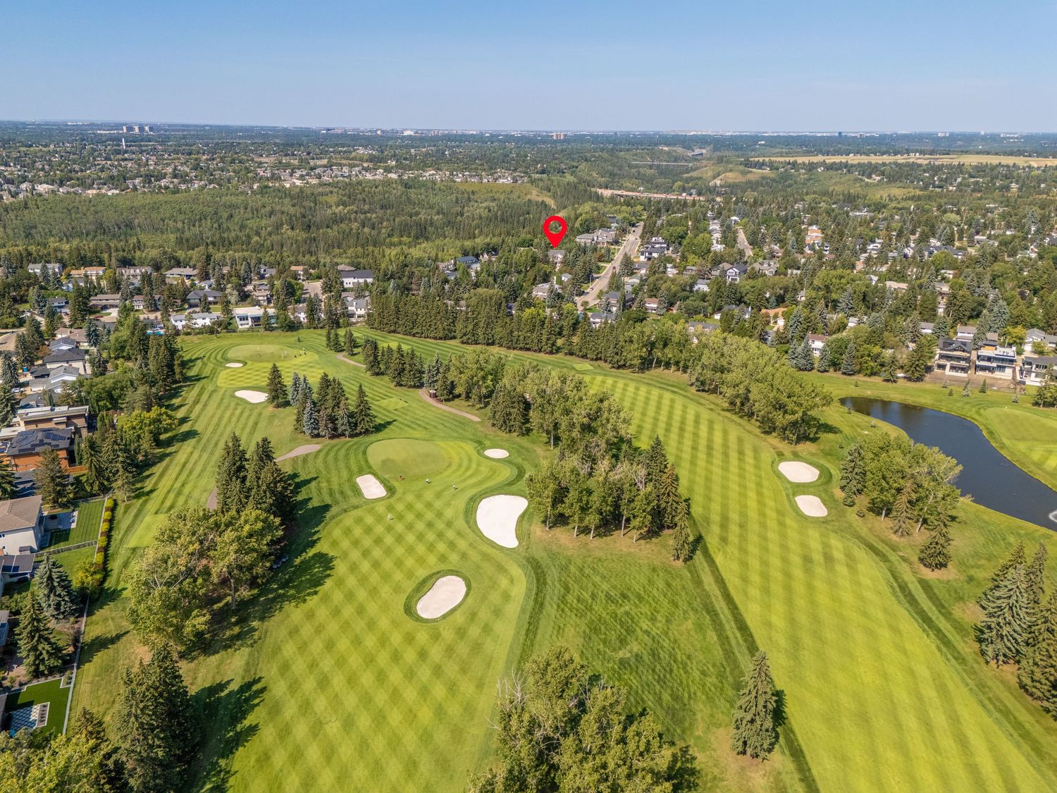 Aerial view of a lush green golf course with sand bunkers, water features, and tree-lined residential neighborhood in background.