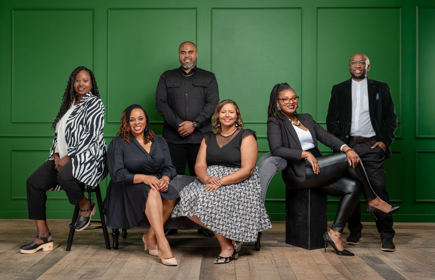 Professional group portrait of team members posed against green paneled wall.