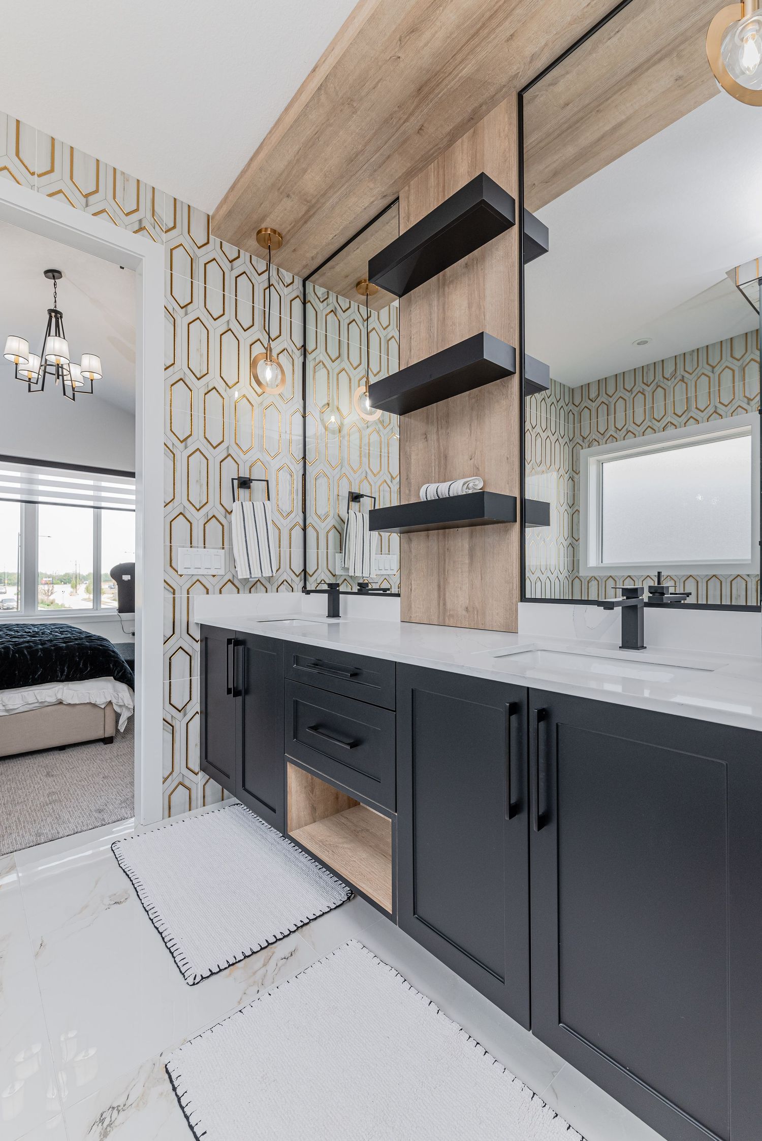 Modern bathroom with dark vanity, dual sinks, black fixtures, open shelving, and geometric wallpaper connecting to a bedroom.