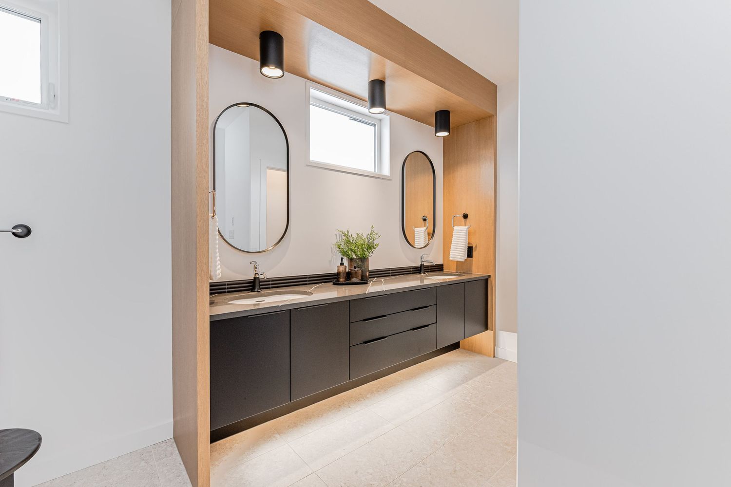 Modern double vanity bathroom with dark cabinets, oval mirrors, and warm wood accent wall.