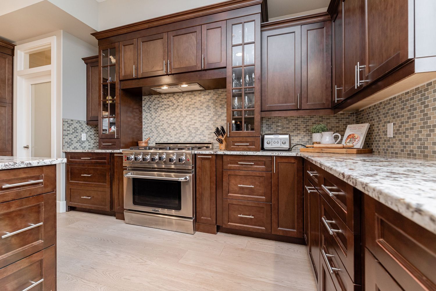 Luxury kitchen with dark wood cabinets, granite countertops, stainless steel range, and mosaic tile backsplash.