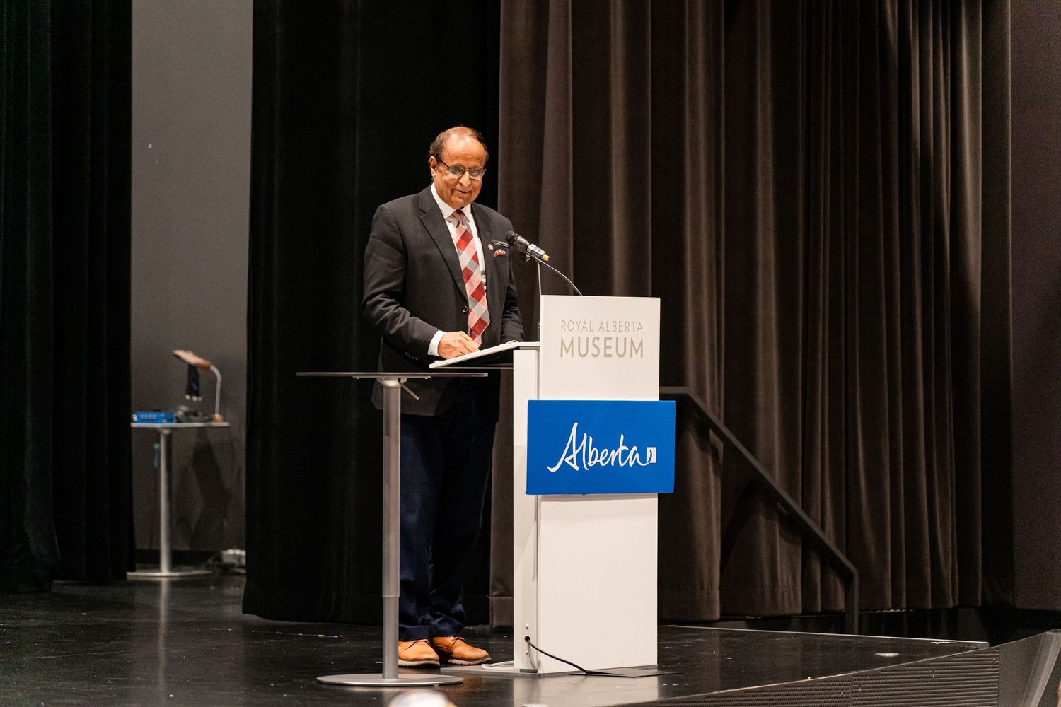 Speaker delivering remarks at Alberta podium on dark stage with professional lighting.