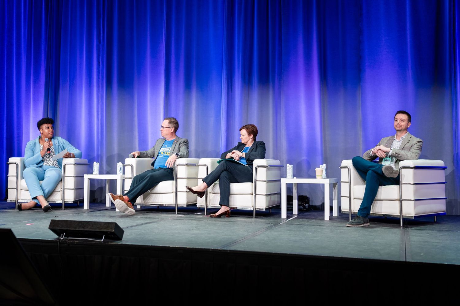 Panel discussion setup with white chairs and tables on conference stage.