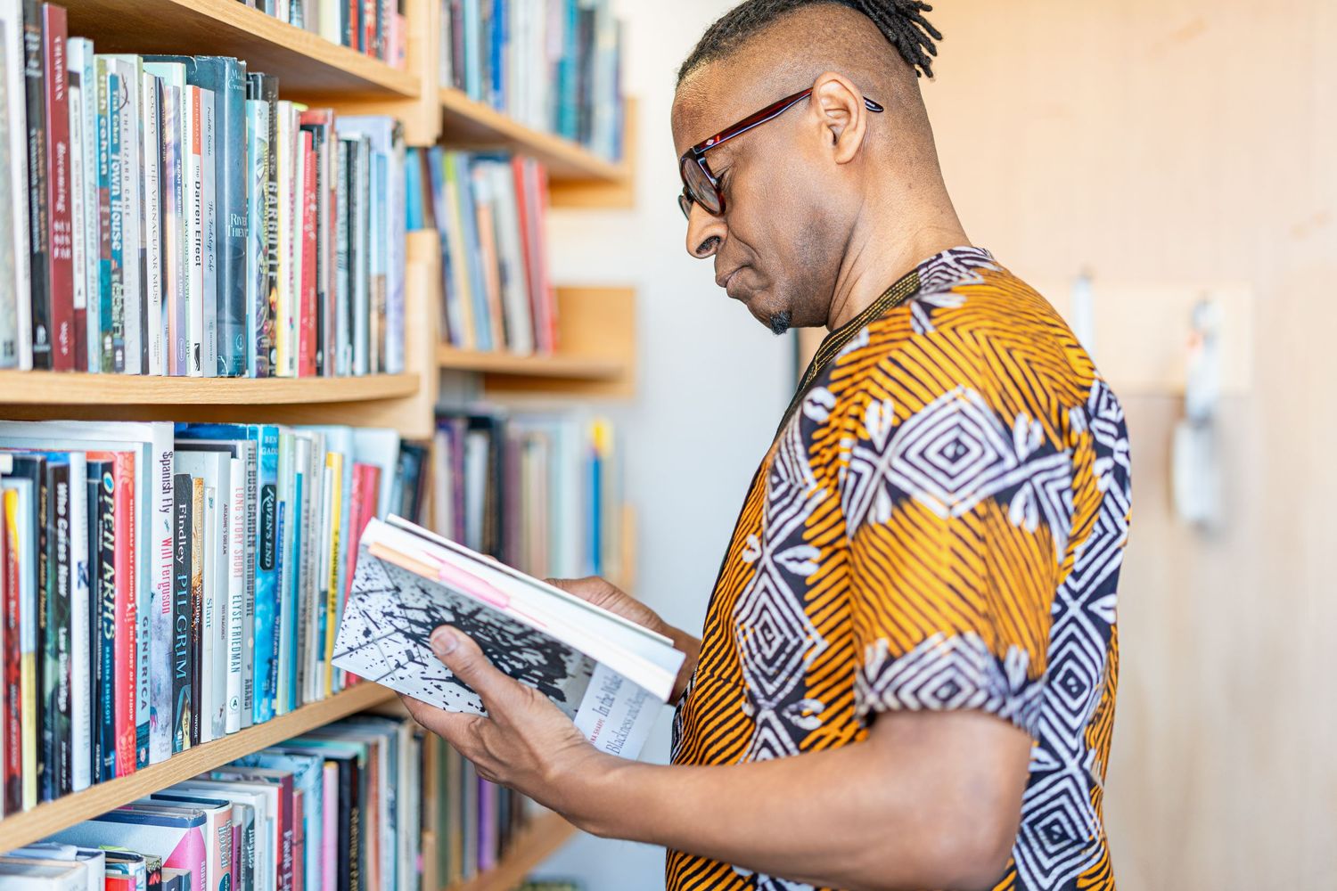 Scholar browsing books in library while wearing traditional African-inspired attire.