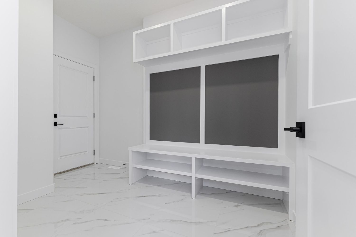 Modern mudroom with white built-in shelving, gray cabinet panels, and marble-look tile flooring.