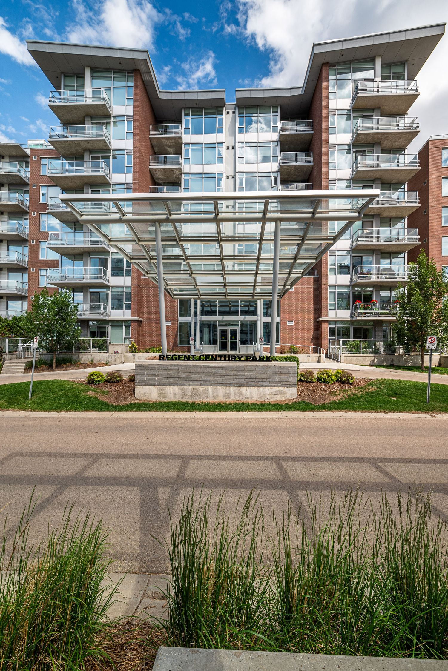 Modern brick condo building with glass canopy entrance, balconies, and landscaped grounds at Regency Century Park.