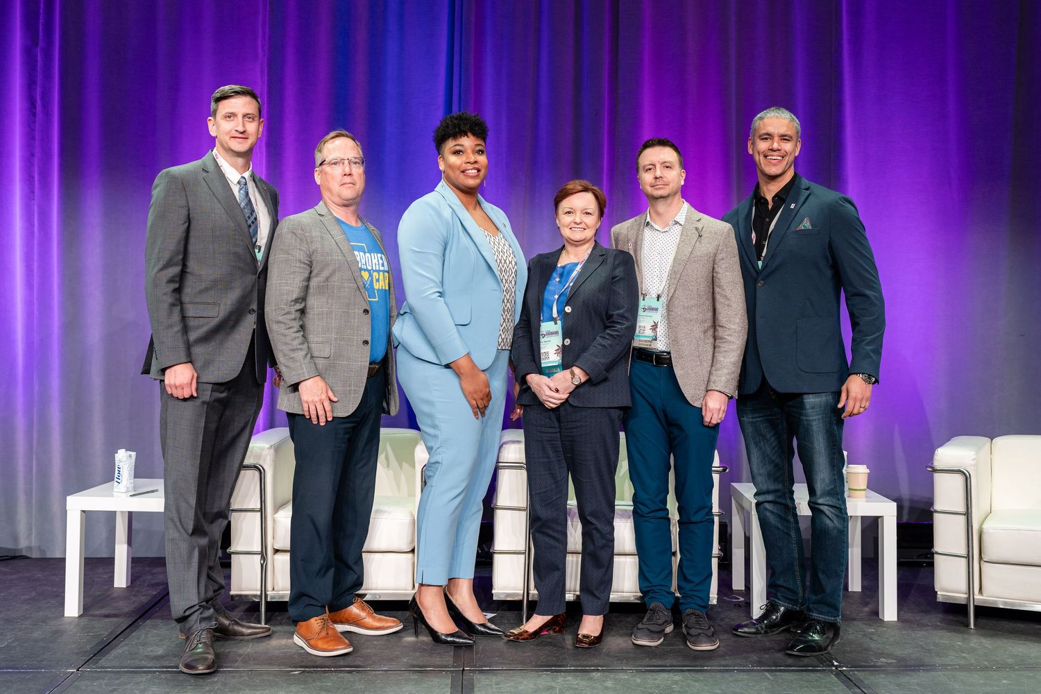 Group photo of conference speakers on stage with blue lighting.