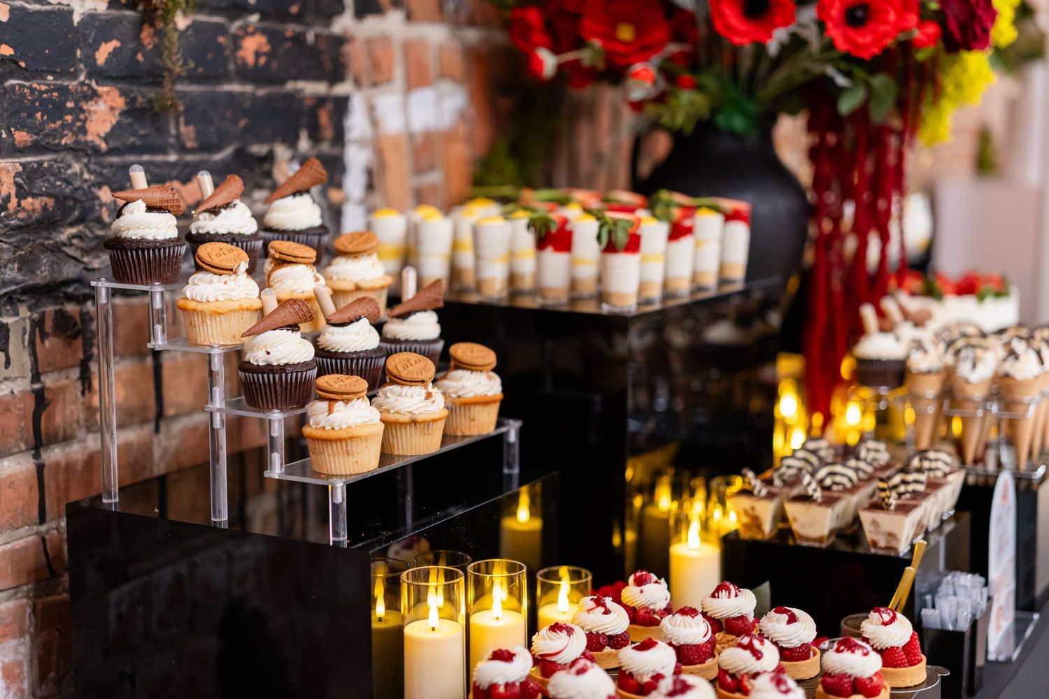 Elegant dessert display featuring tiered stands of mini cupcakes and treats illuminated by candlelight.
