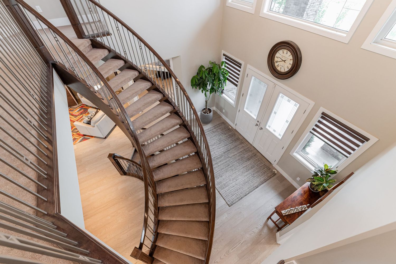 Elegant curved staircase with dark wood railings overlooking a bright two-story foyer with hardwood floors.