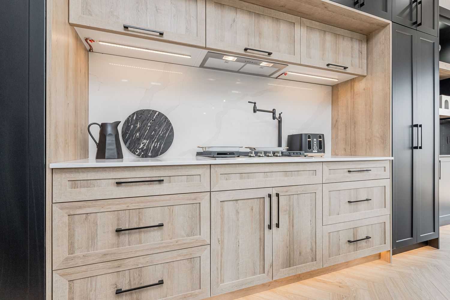 Modern kitchen with light wood shaker cabinets, black hardware, white countertops, and a built-in gas cooktop with pot filler.