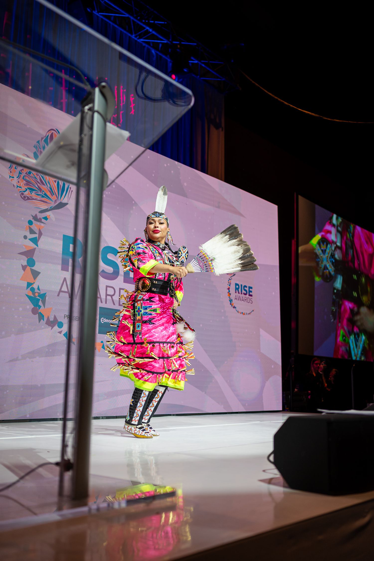 Performer in bright pink outfit dancing on illuminated stage during fashion show.