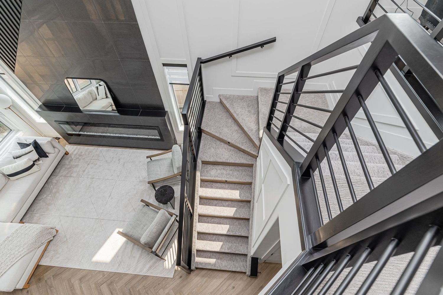 Aerial view of modern staircase with dark metal railings and light carpet treads in a bright contemporary home.