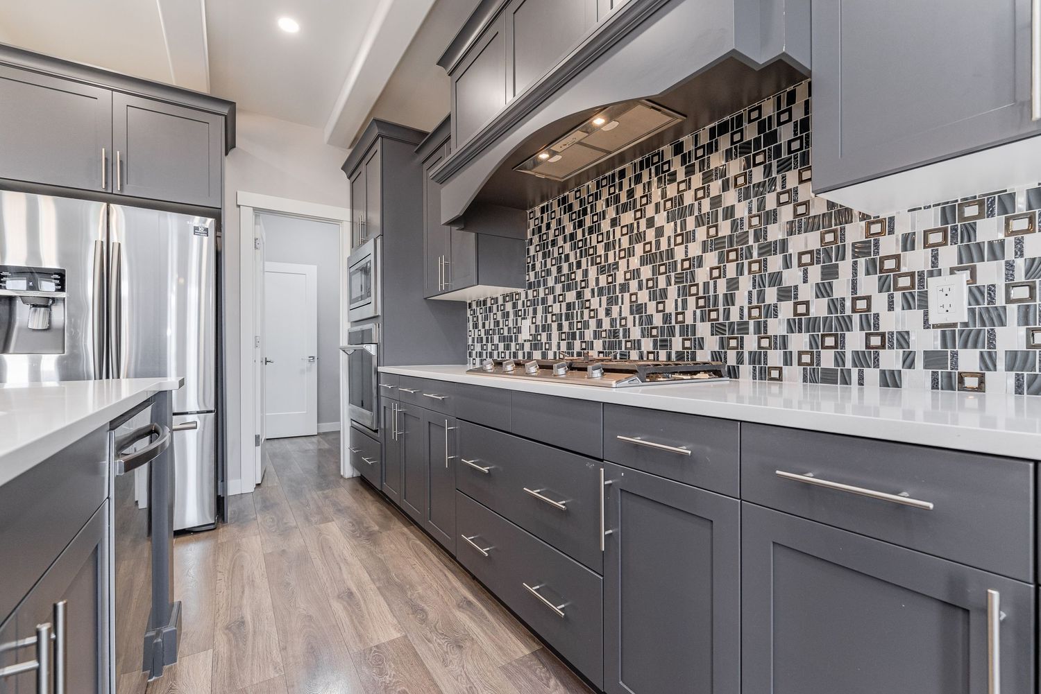 Modern kitchen with gray cabinets, mosaic tile backsplash, white countertops, and hardwood floors.