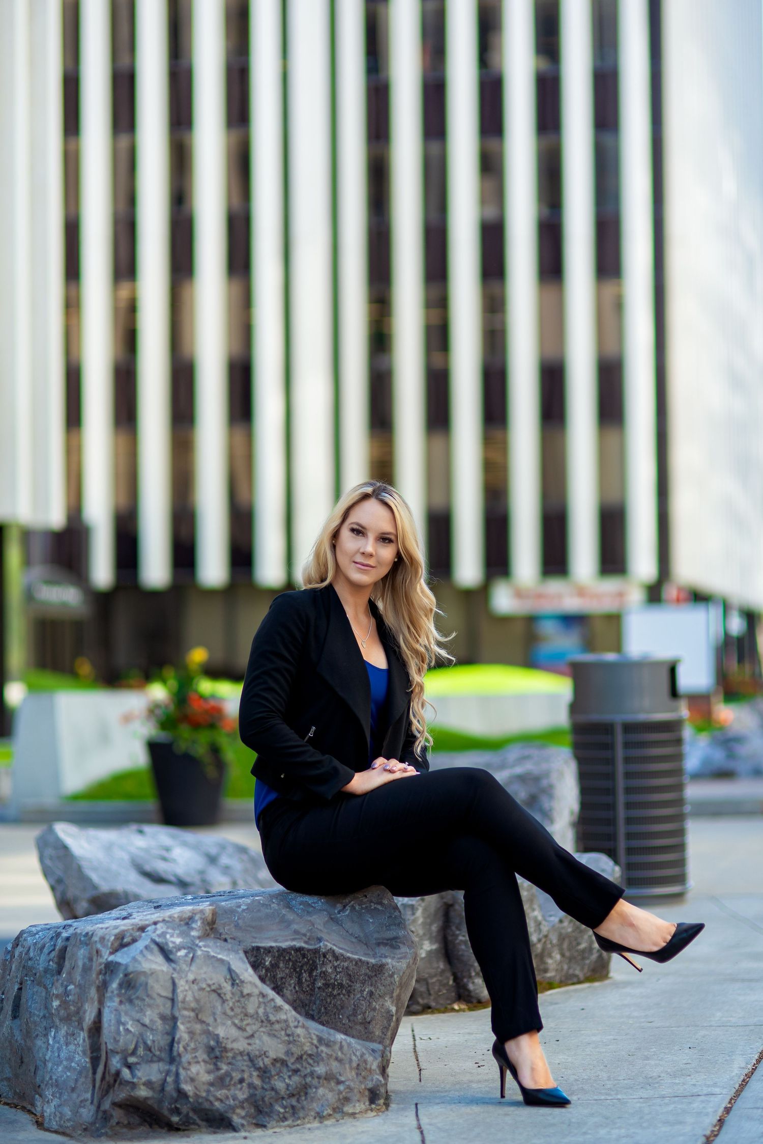 Business woman in professional attire sitting on stone blocks near modern office building.