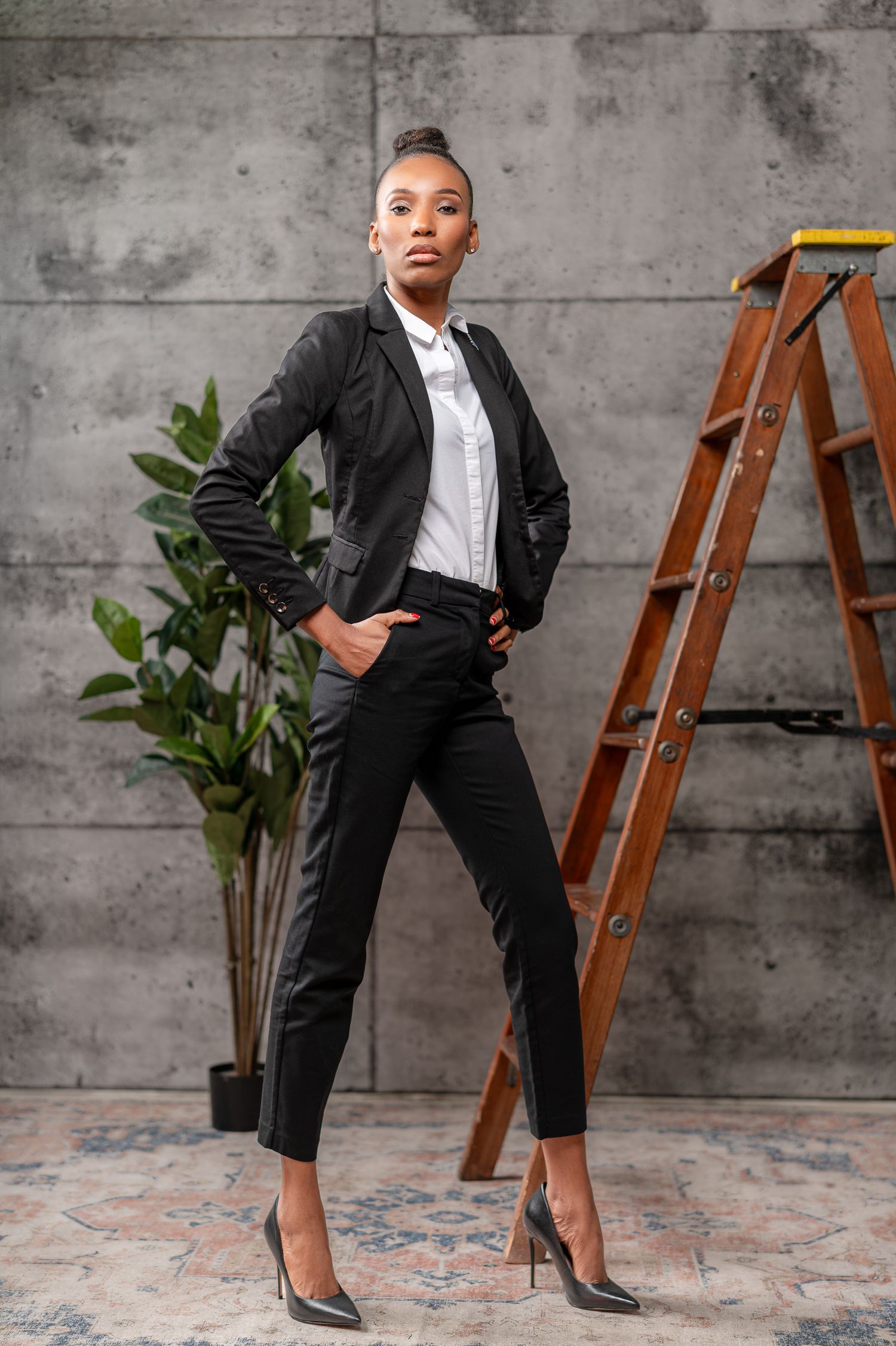 Modern business poses with leather ladder and plants against concrete wall.