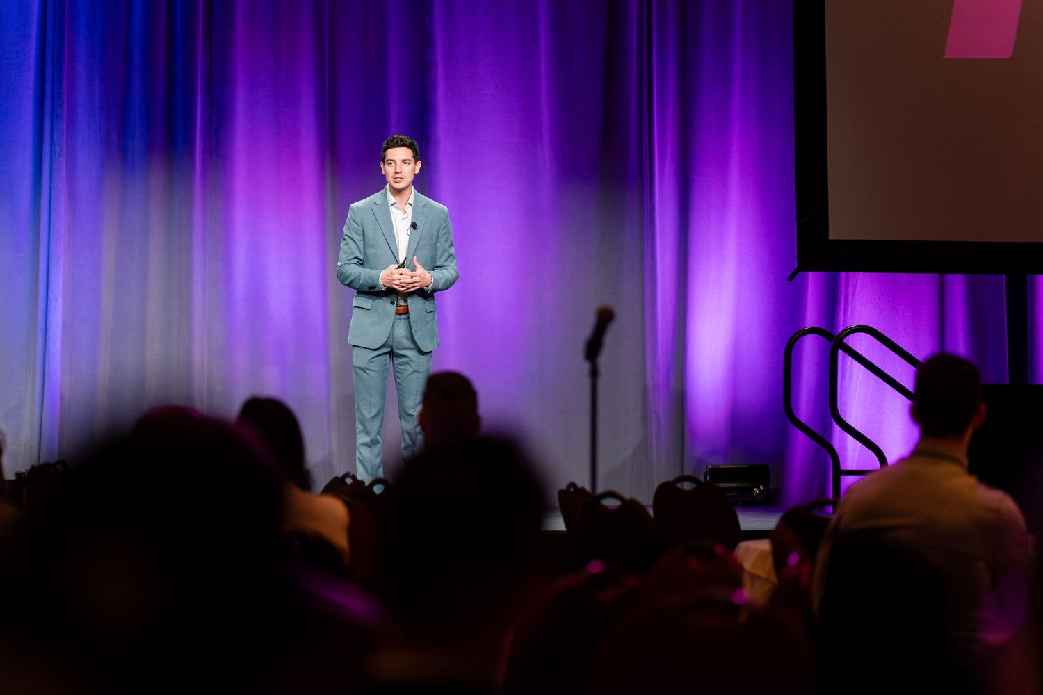 Professional conference presentation on stage with purple-lit backdrop.