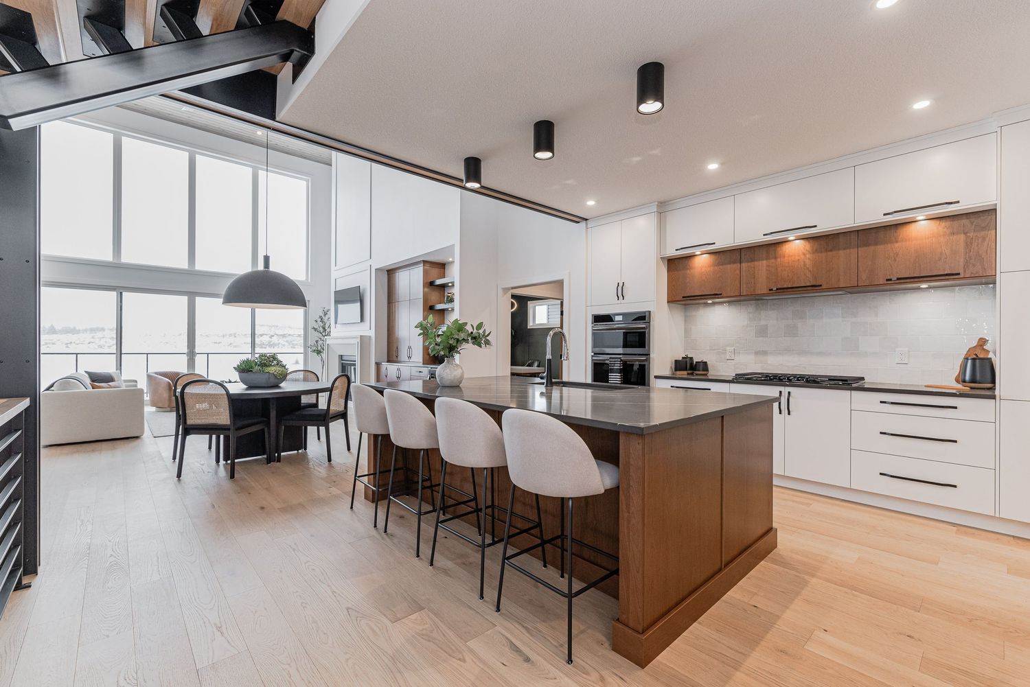 Modern open-concept kitchen with white cabinets, dark island, bar stools, and hardwood floors leading to dining area.