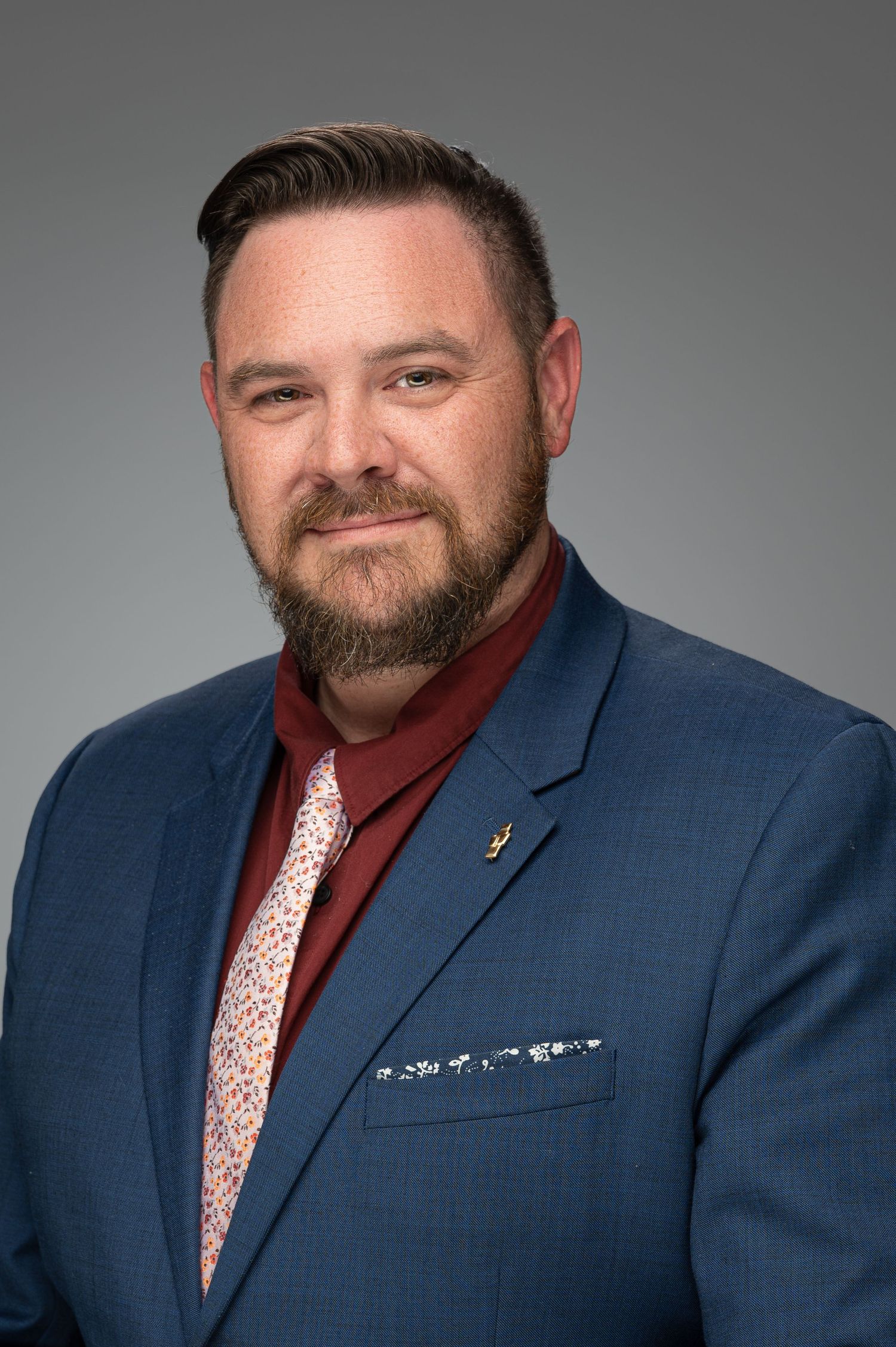 Business portrait of person wearing navy suit and burgundy shirt with patterned tie.