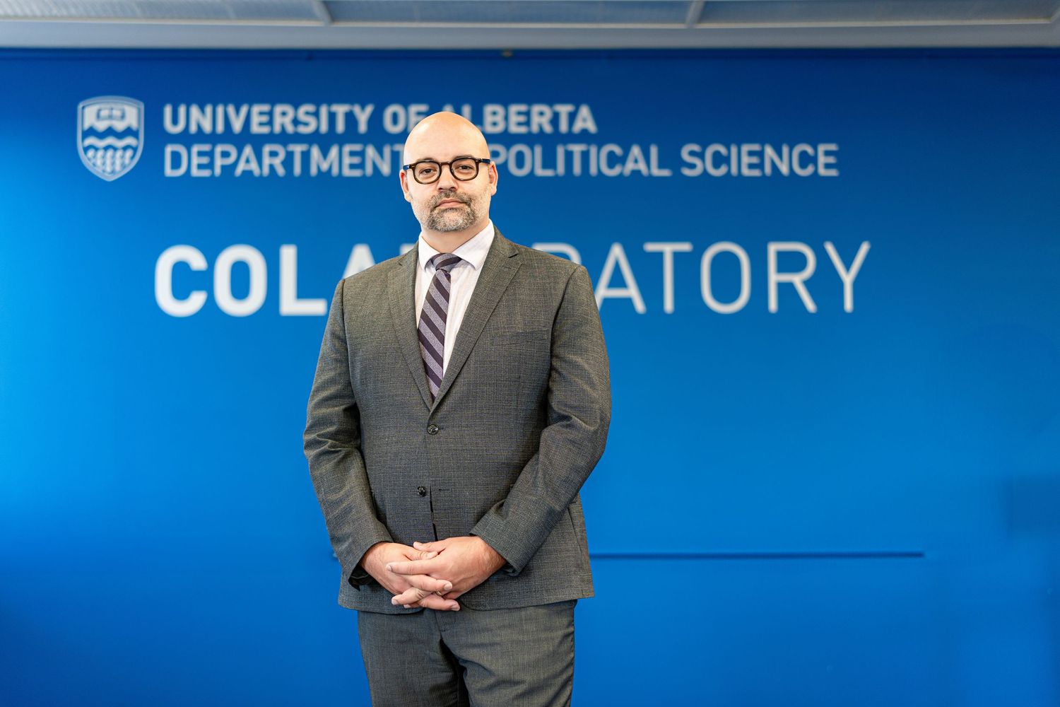 Professor standing in front of University of Alberta Department of Political Science Collaboratory sign.