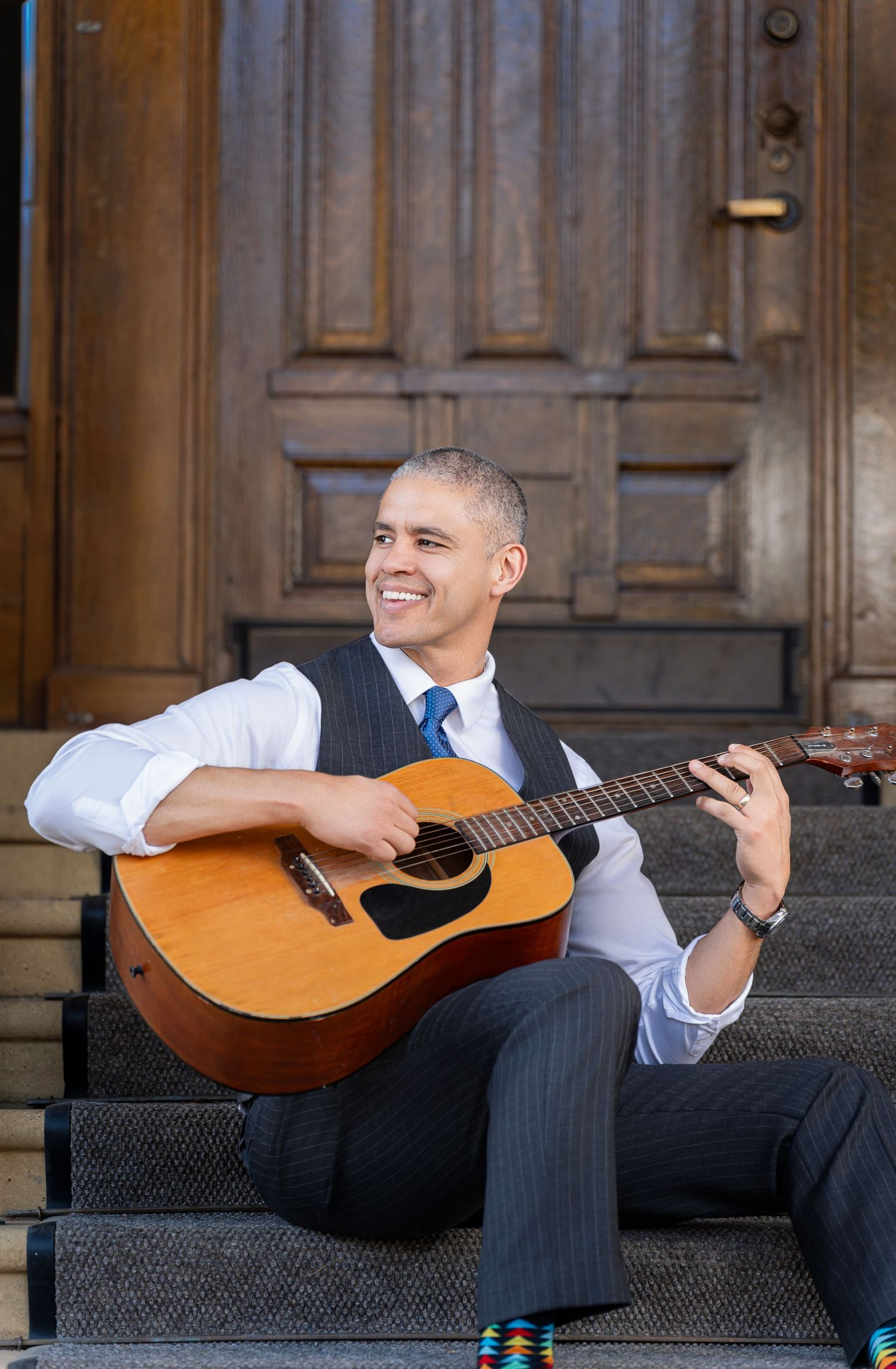 Musician playing acoustic guitar while sitting on outdoor stone steps.