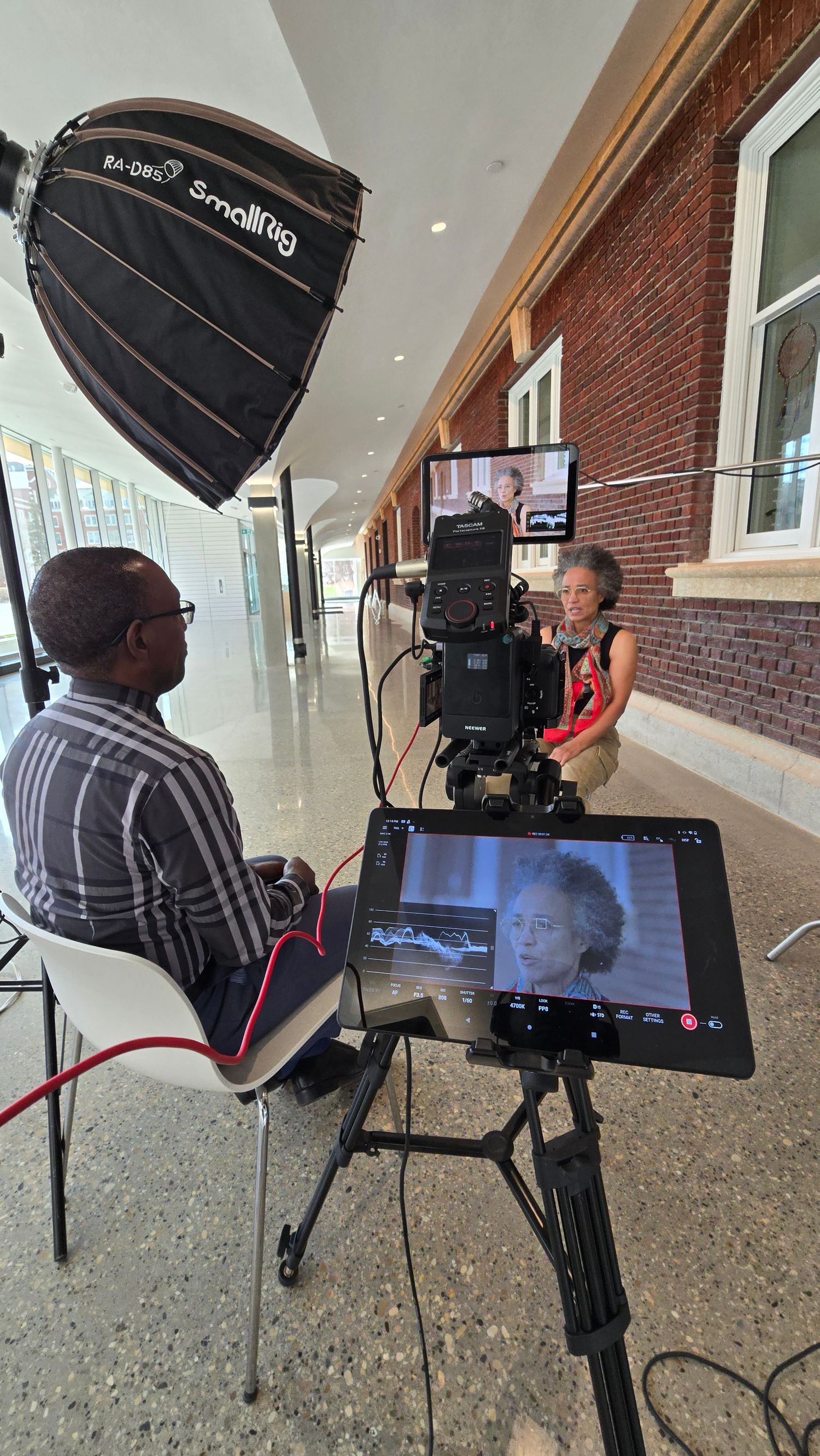 Behind-the-scenes photo shoot setup with lighting equipment and monitors in a brick-walled hallway.