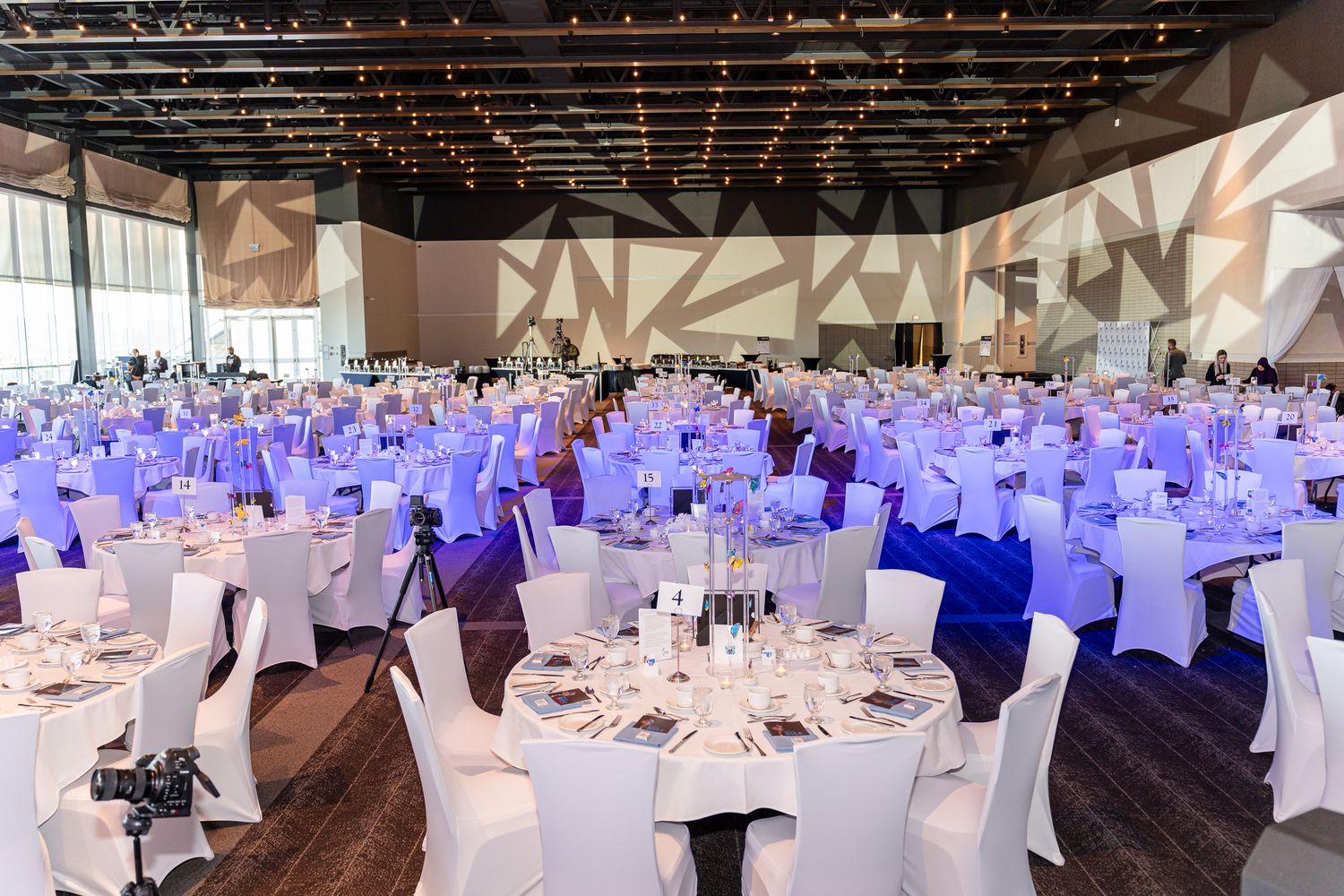 Large banquet hall setup with white tablecloths and blue lighting for formal event.