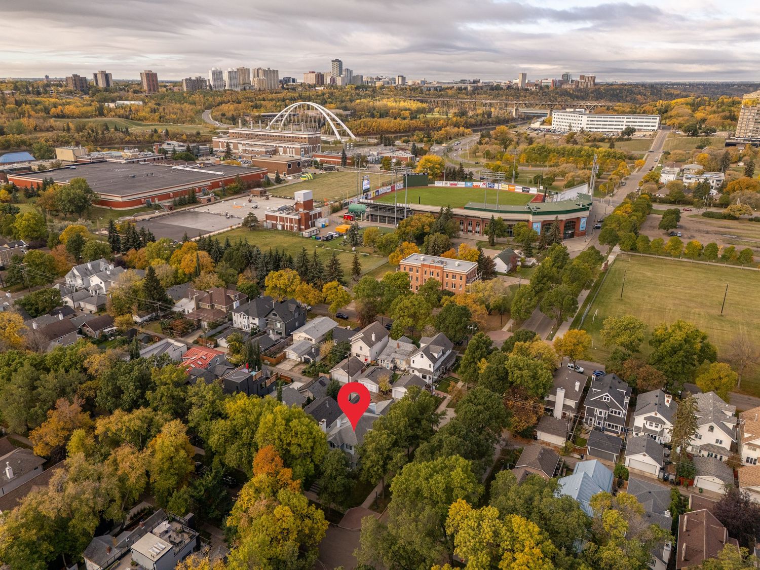 Aerial view of Edmonton residential neighborhood with colorful autumn trees, the iconic Walterdale Bridge, and city skyline in background.