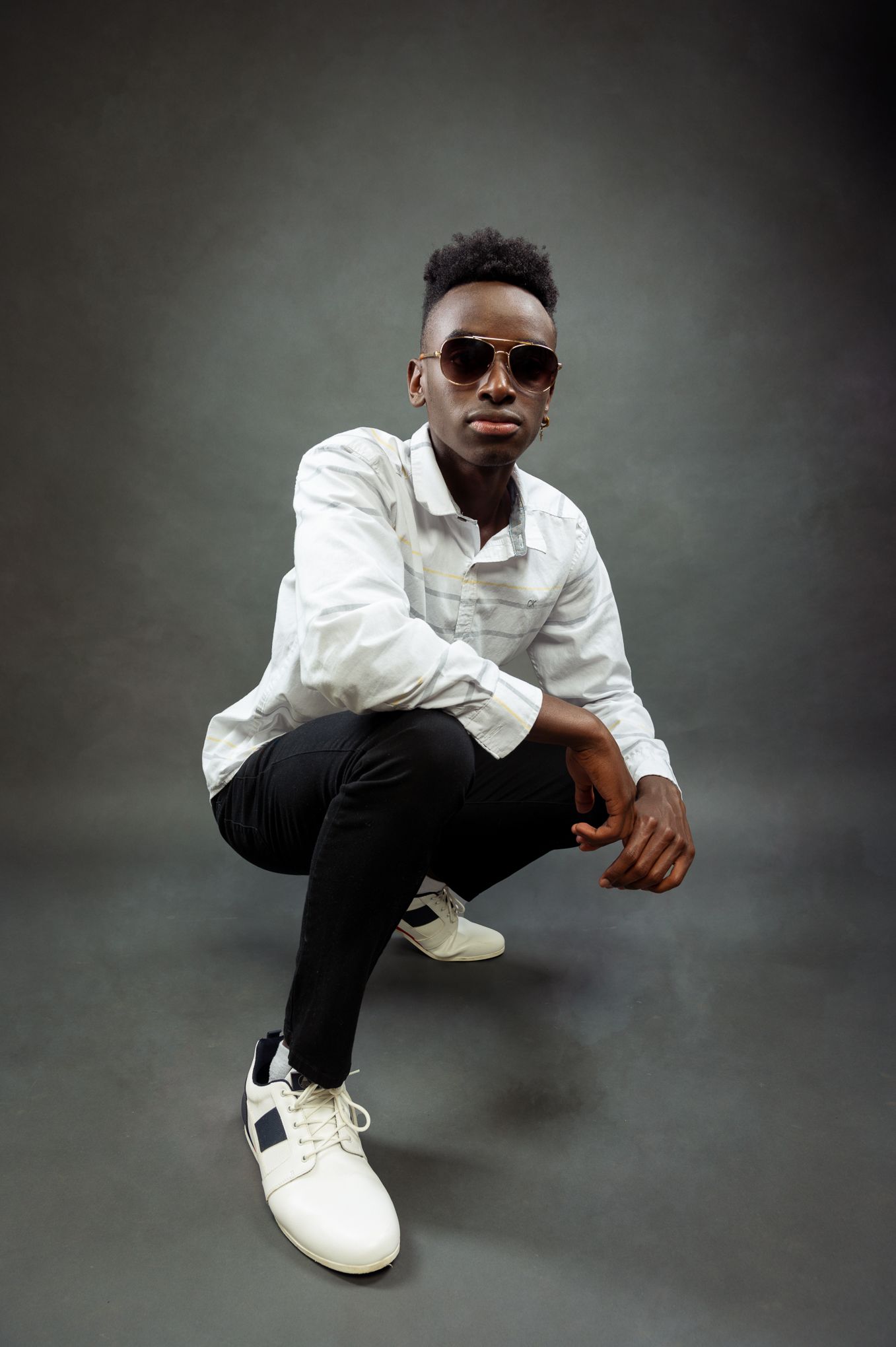 Stylish studio portrait with model crouching in white shirt against dark backdrop.