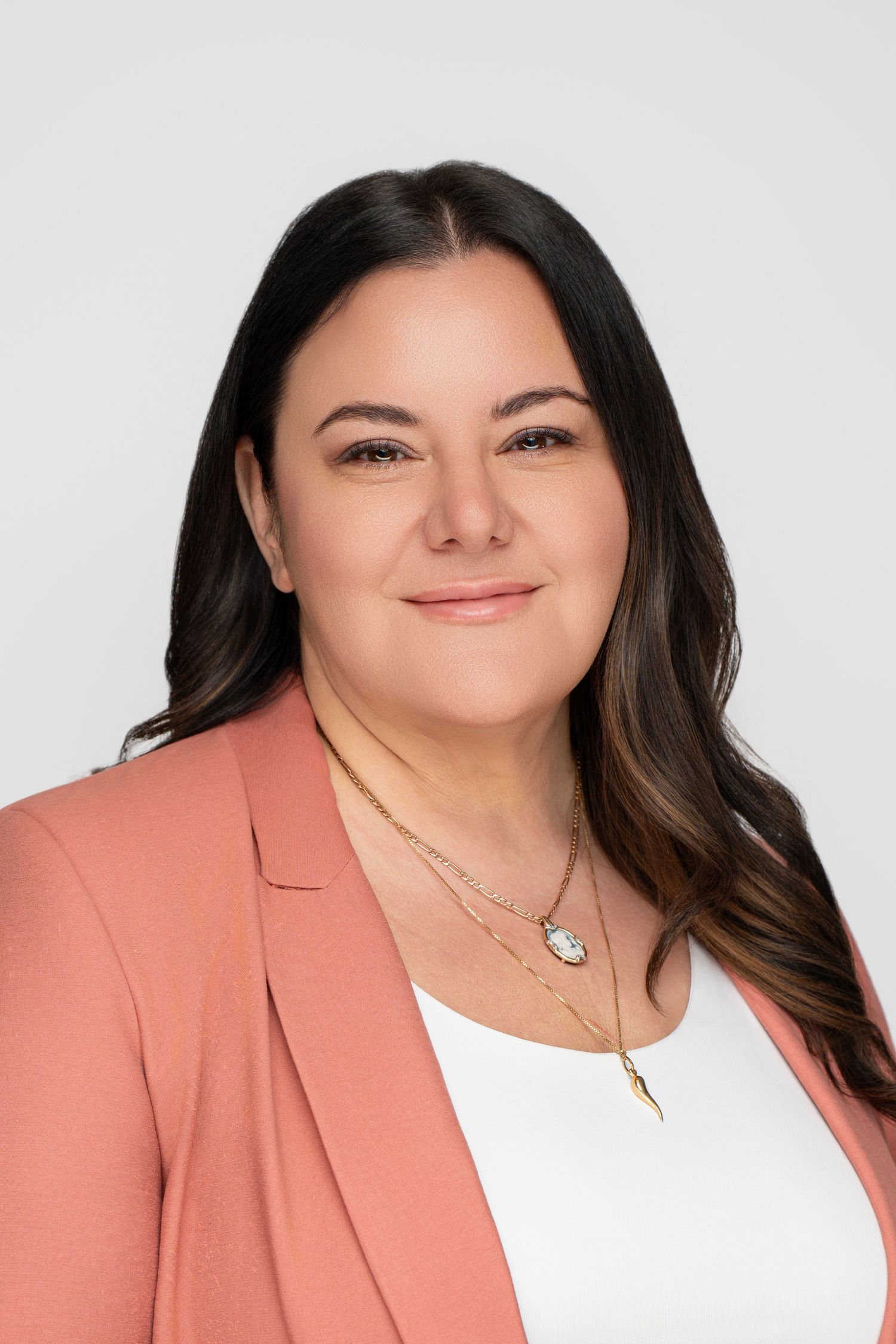 Professional headshot of person in coral blazer and white top against white background.