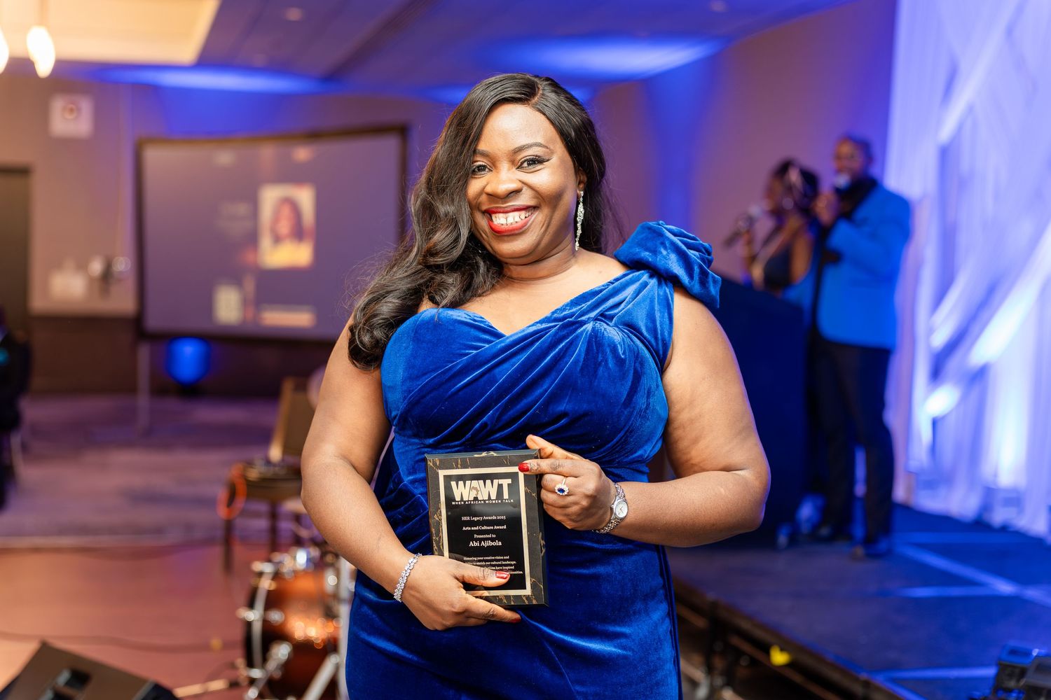 Attendees in royal blue attire at an awards ceremony with blue lighting effects.