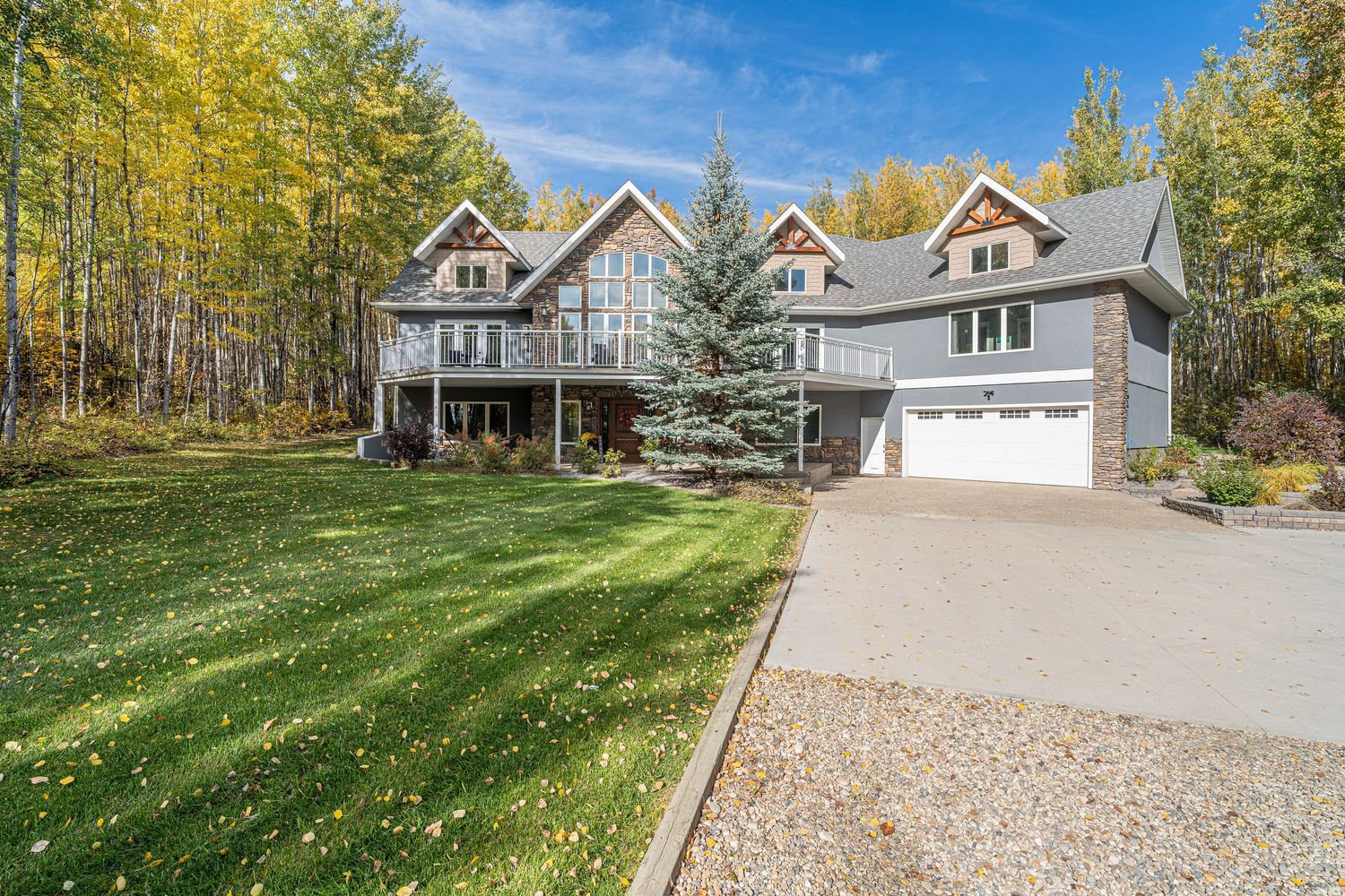Large two-story craftsman home with triple garage, manicured lawn, and mature trees displaying vibrant fall foliage.