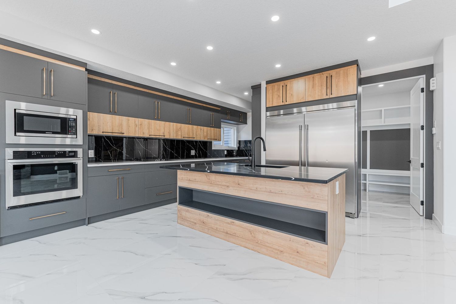 Modern kitchen with gray cabinets, wood accents, marble floors, stainless steel appliances, and a large center island.