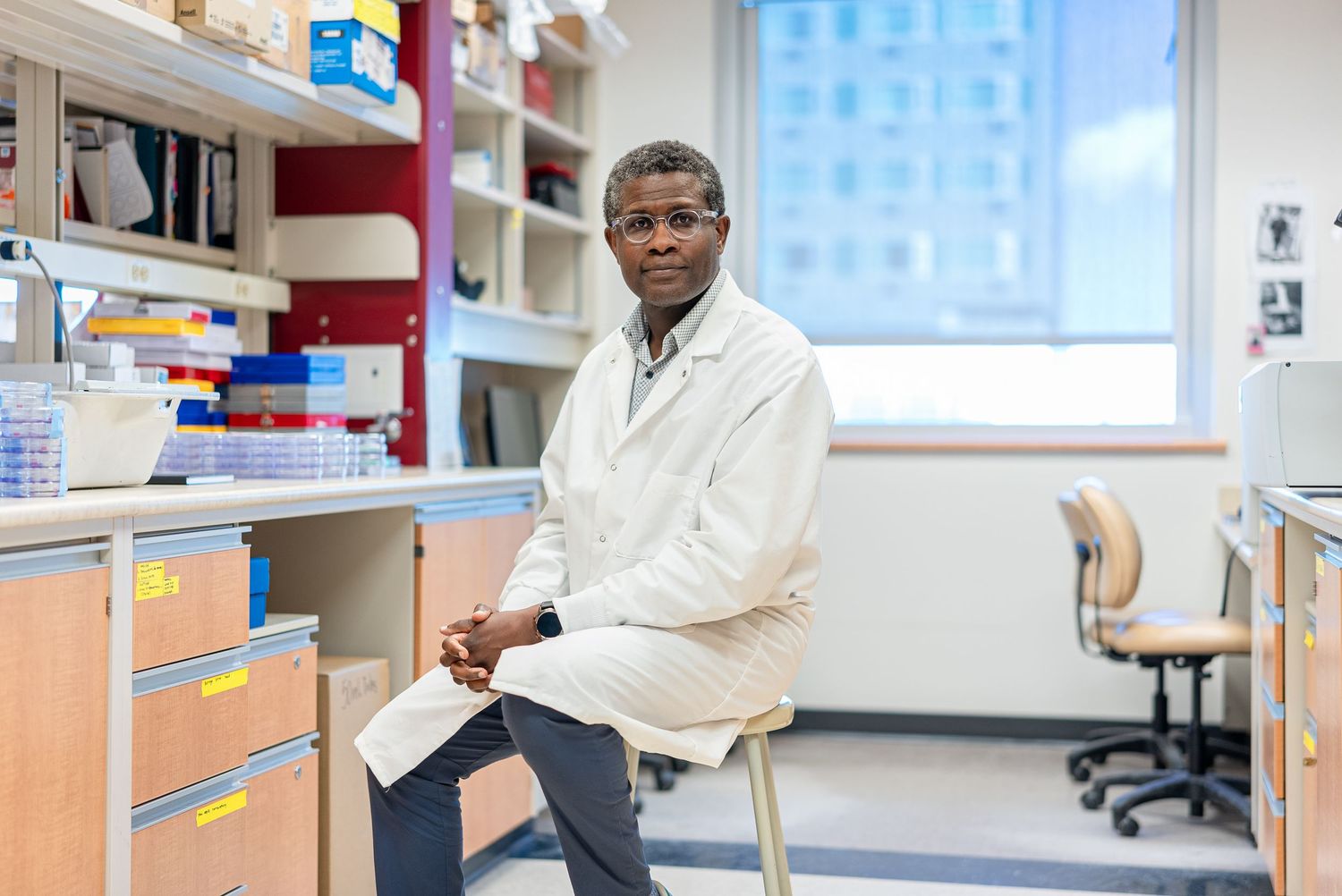 Researcher in white coat sits at laboratory workstation.