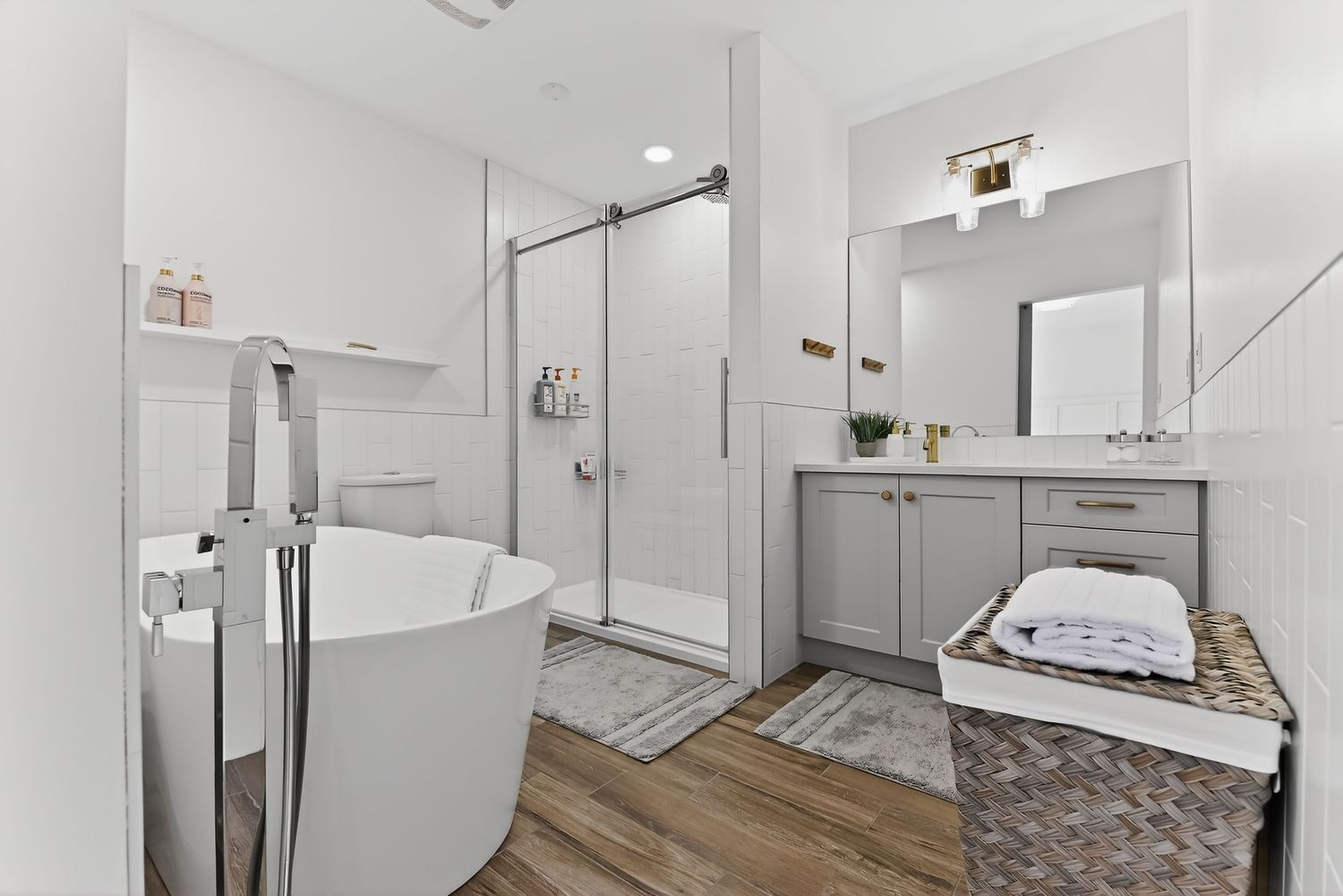 Modern bathroom with freestanding soaking tub, glass walk-in shower, gray vanity, and wood-look flooring.