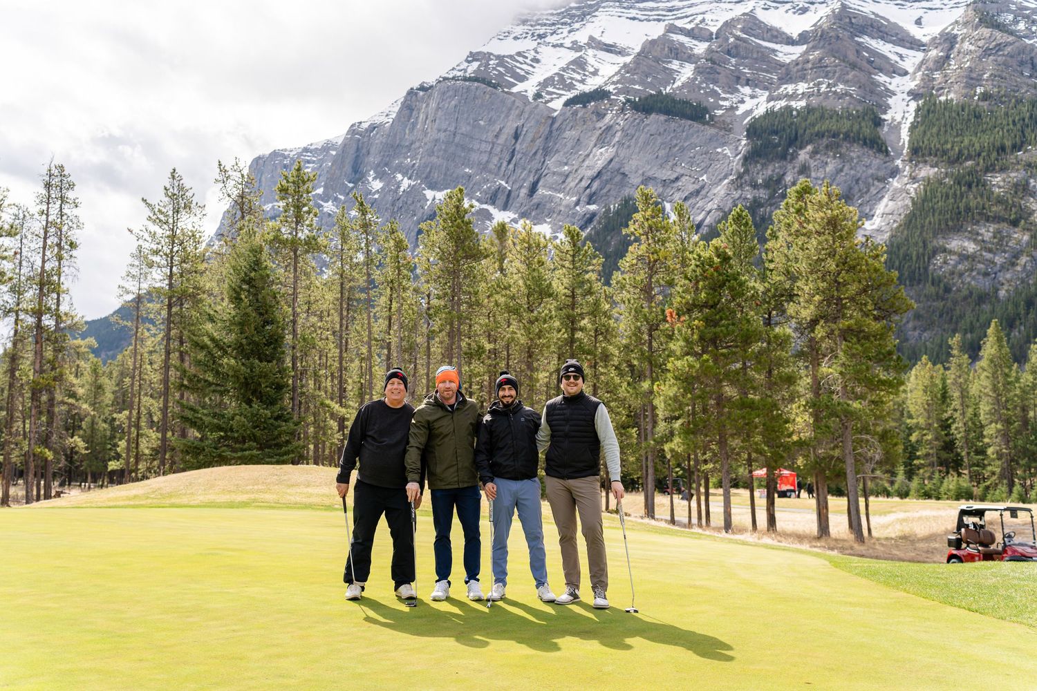 Group stands on a golf course with majestic mountain peaks and evergreen forest in the background.