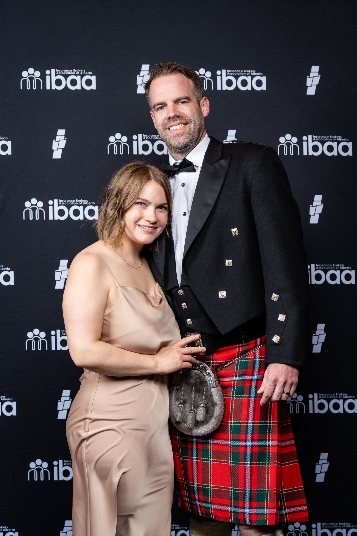 Event photos against IBAA step-and-repeat backdrop featuring formal attire and traditional Scottish kilt.