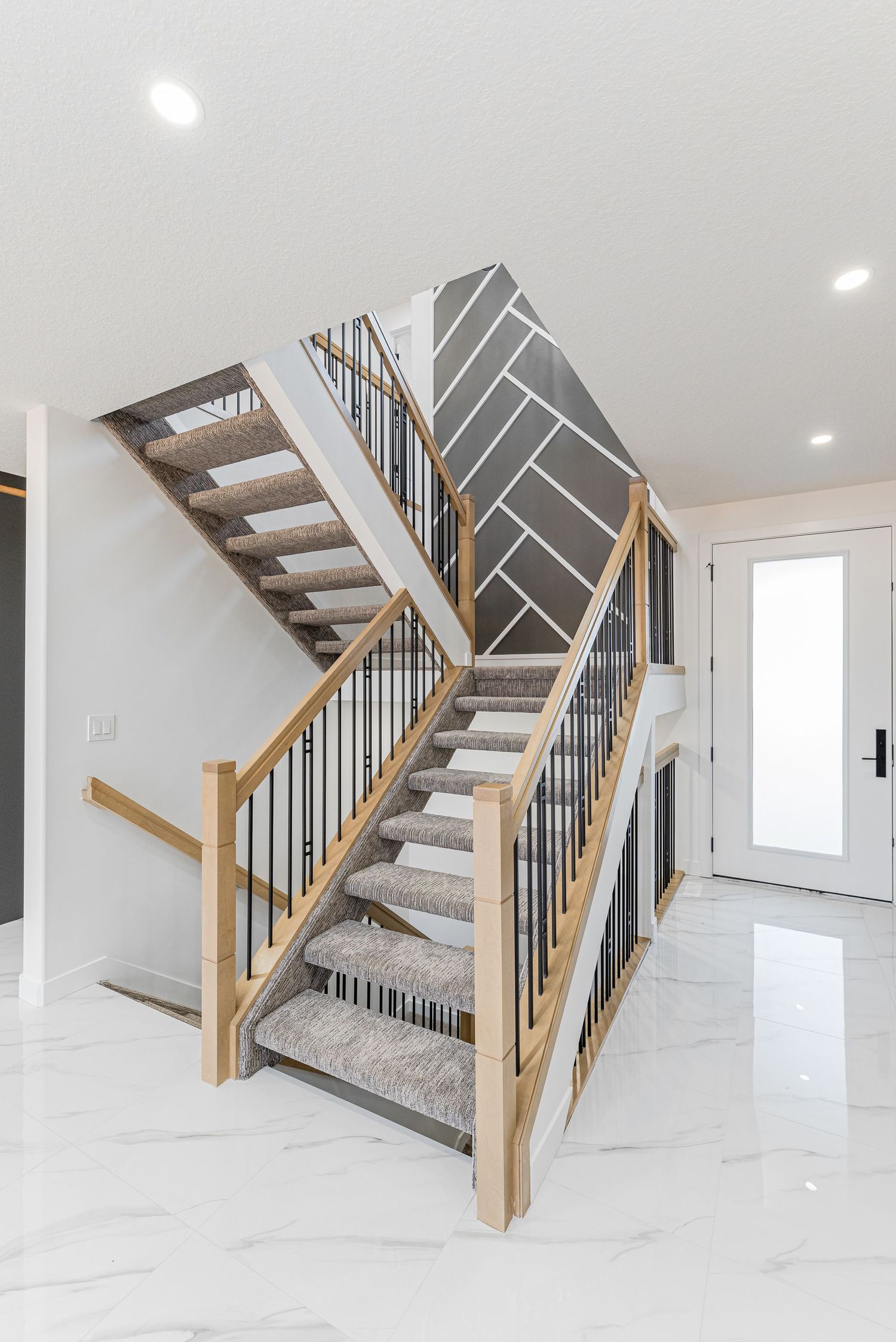Modern staircase with wood railings, black metal balusters, carpet treads, and geometric accent wall in bright white home.