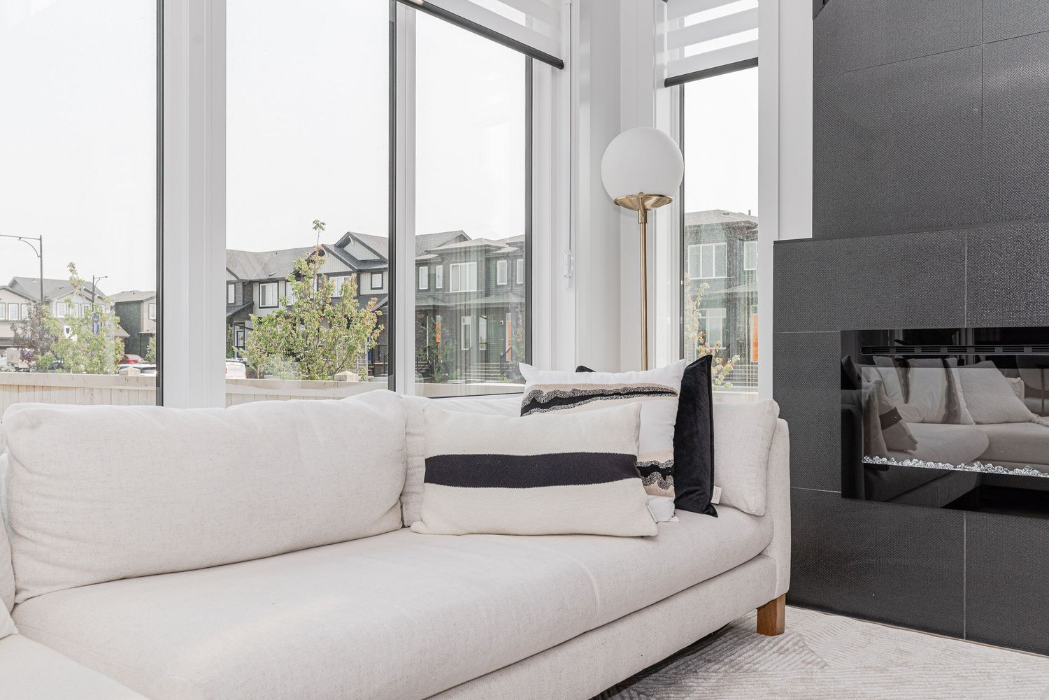 Modern living room with white sofa, globe floor lamp, large windows, and dark tile fireplace.