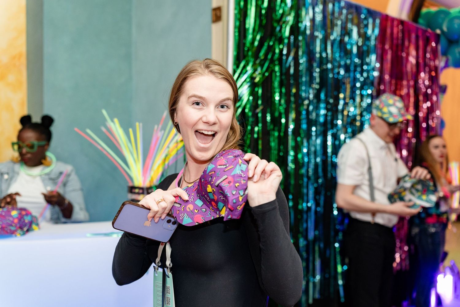 Colorful party scene with sparkly decorations and someone holding glow sticks against a metallic fringe backdrop.
