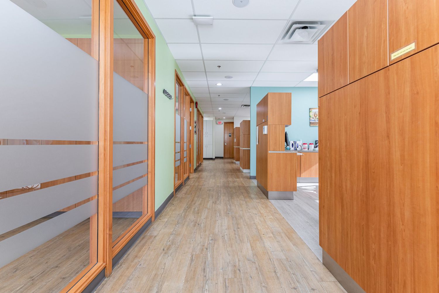 Long hallway in dental office featuring wooden cabinets and modern lighting fixtures.