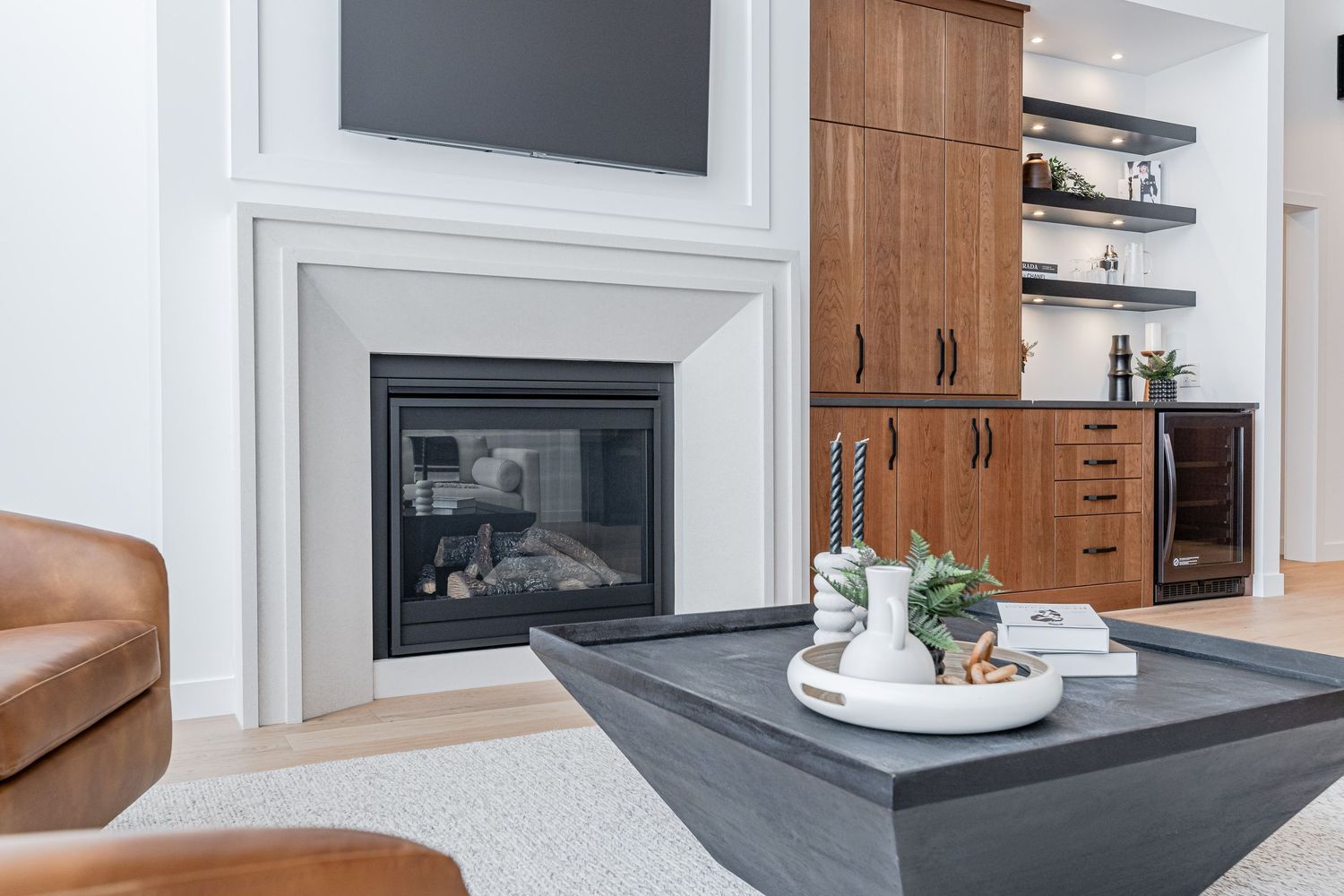 Modern living room with a white fireplace, walnut built-ins, leather chair, and a dark concrete coffee table.