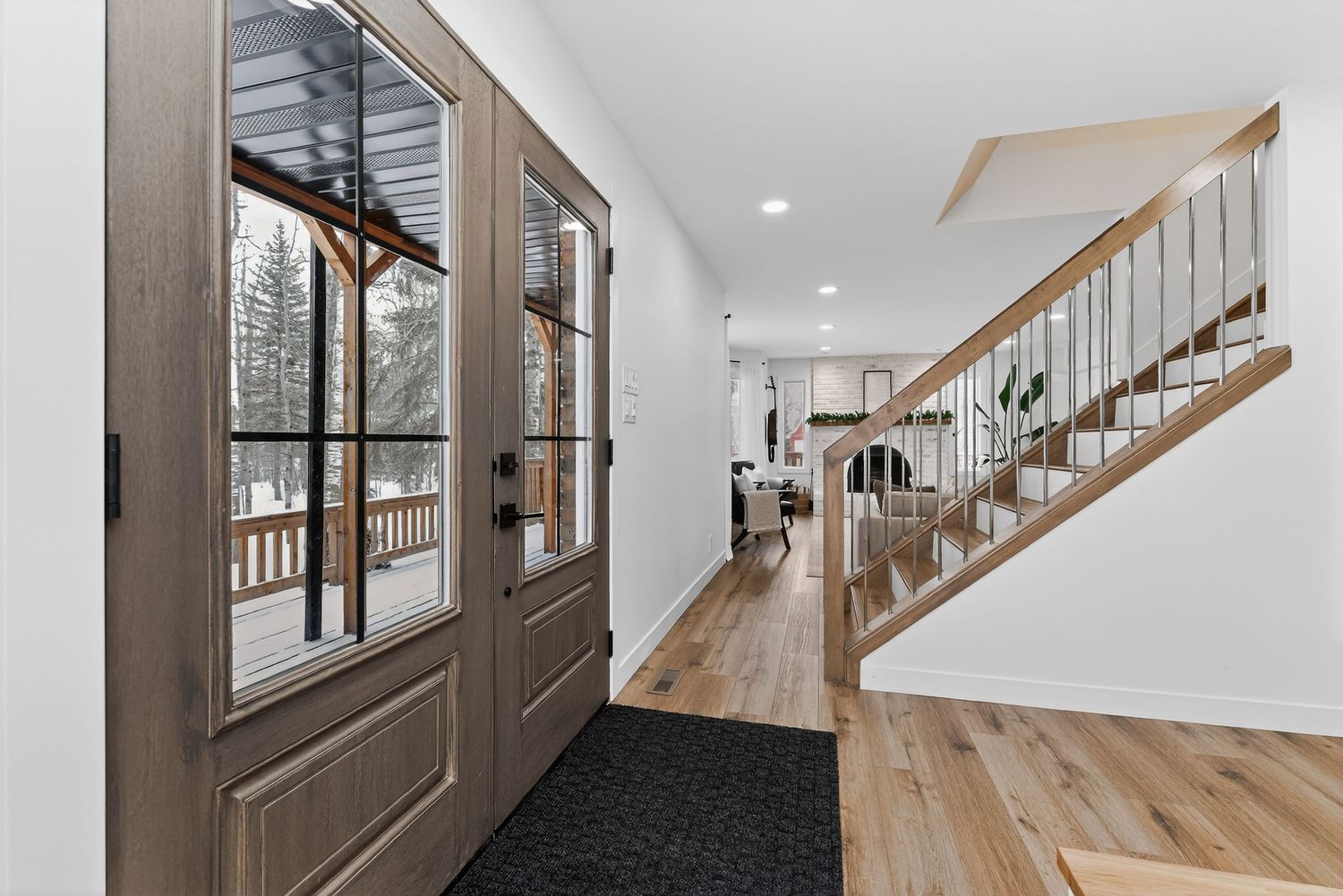 Modern entryway with wood-framed glass door, light hardwood floors, black mat, and open staircase with white balusters.