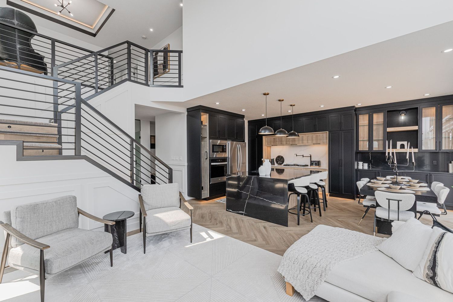 Modern open-concept living space with black kitchen, white sofas, and industrial staircase railing.