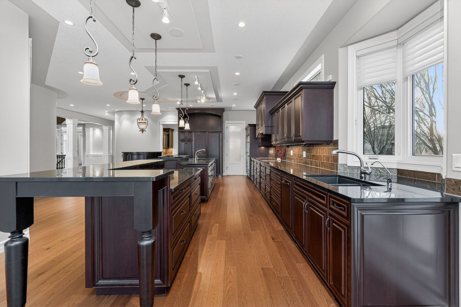 Spacious kitchen with dark wood cabinets, granite countertops, large island, pendant lights, and hardwood floors.