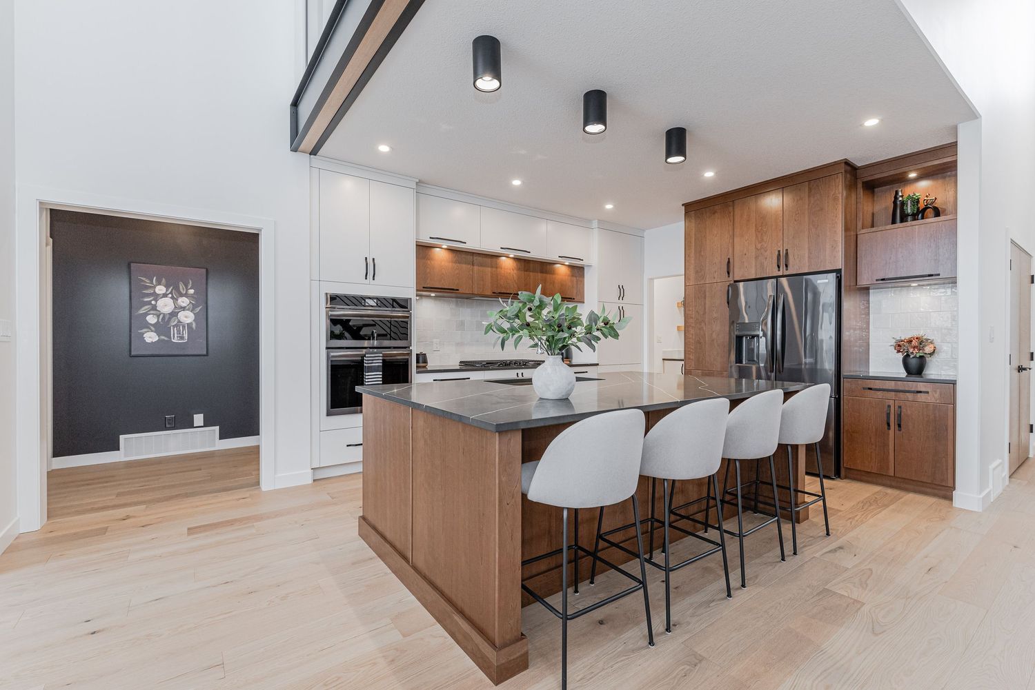 Modern open-concept kitchen with walnut cabinetry, white island, bar stools, stainless appliances, and light hardwood floors.