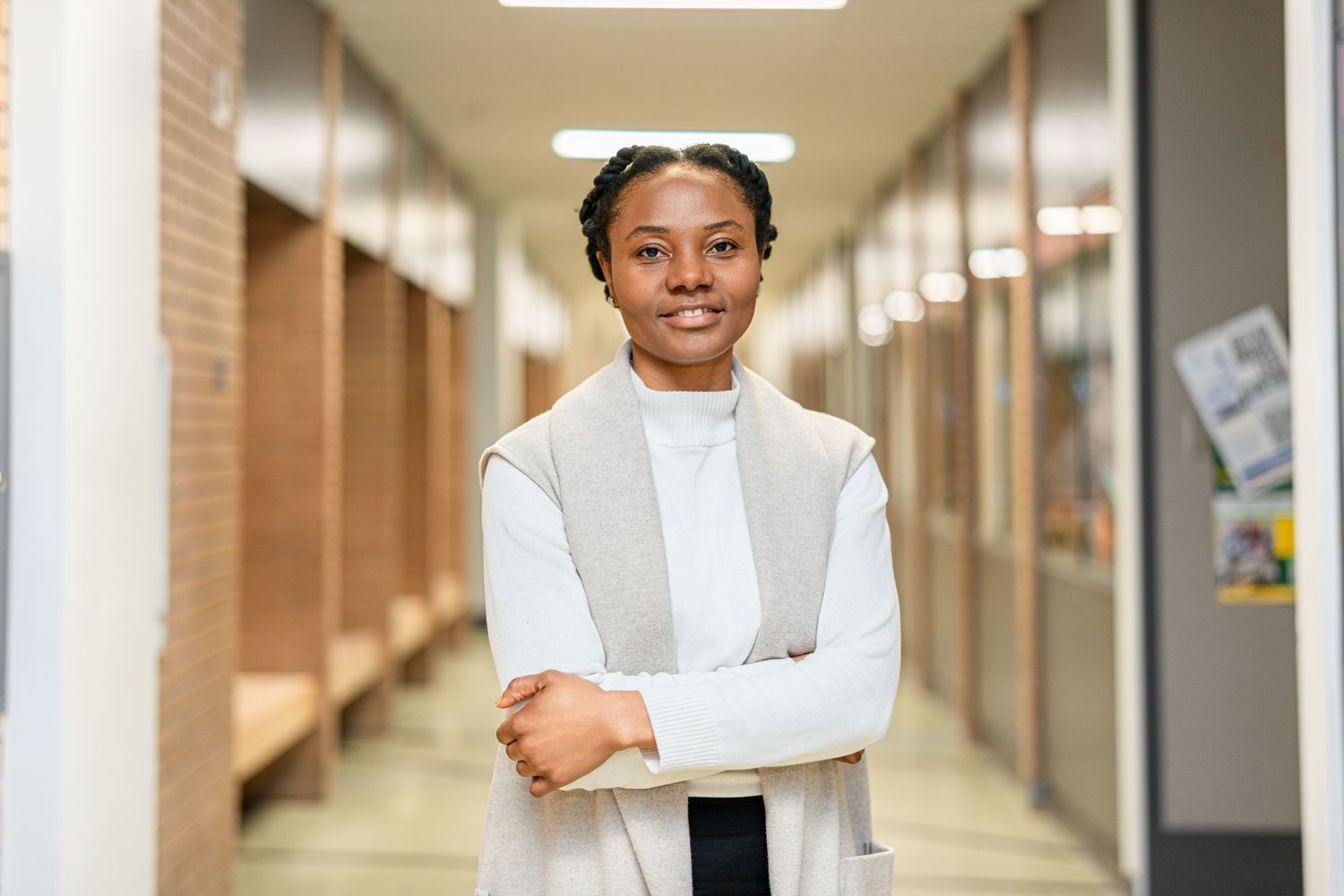 Student in cream sweater stands confidently in school hallway.