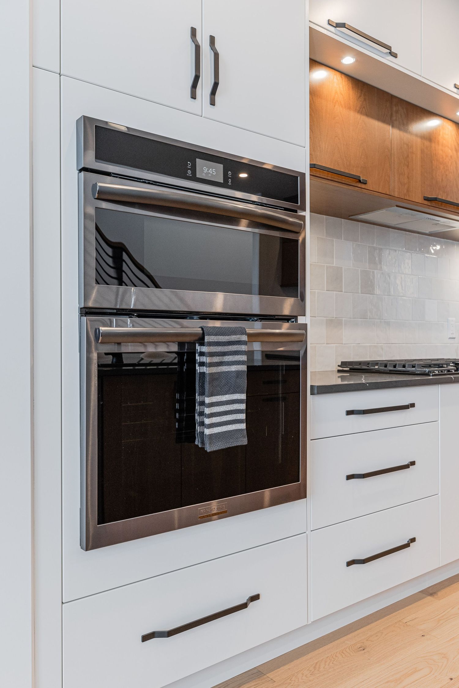 Modern kitchen with stainless steel double wall oven, white cabinetry, dark handles, and subway tile backsplash.