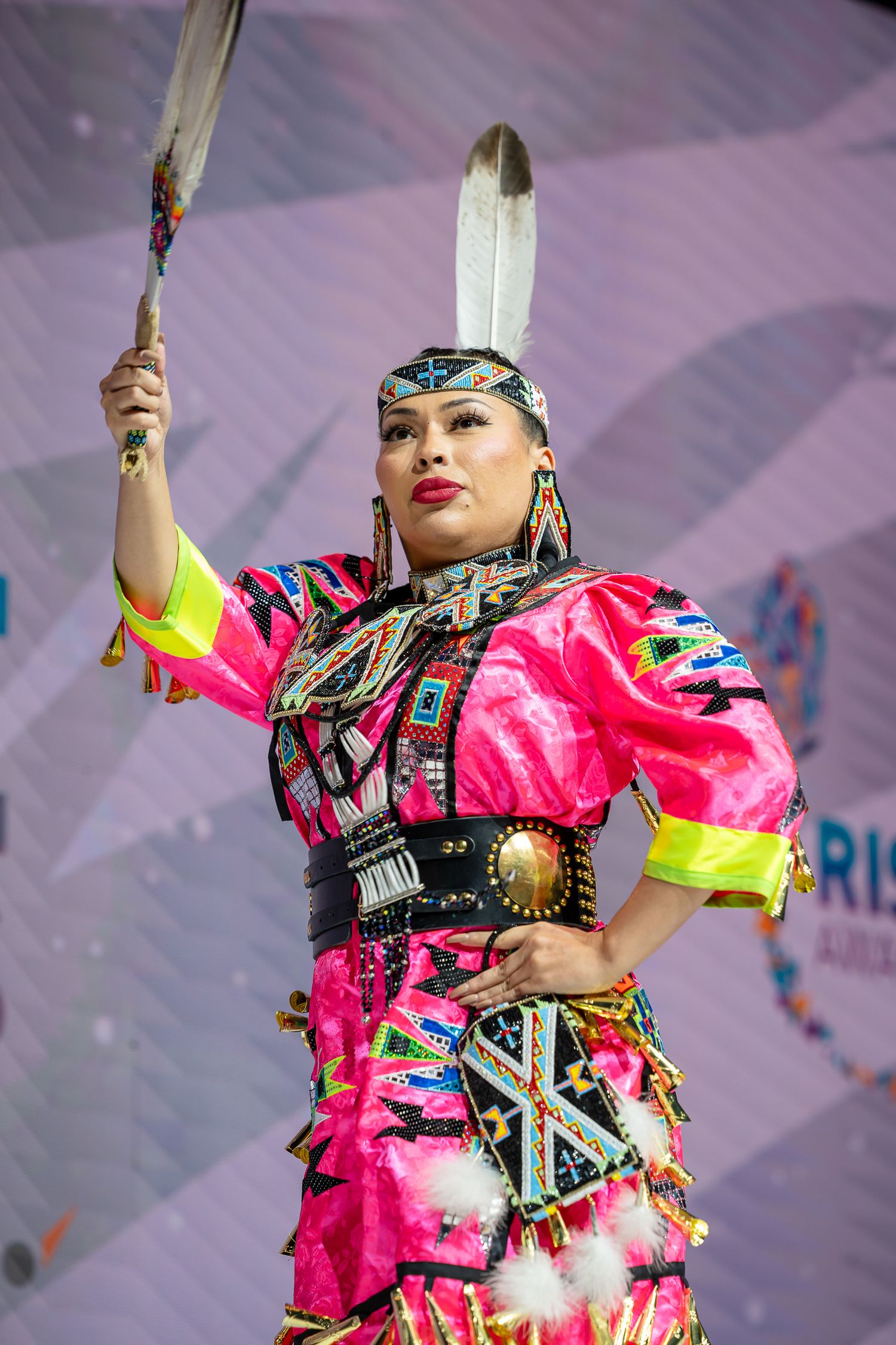 Traditional dancer performs in vibrant pink regalia with yellow accents during cultural celebration.